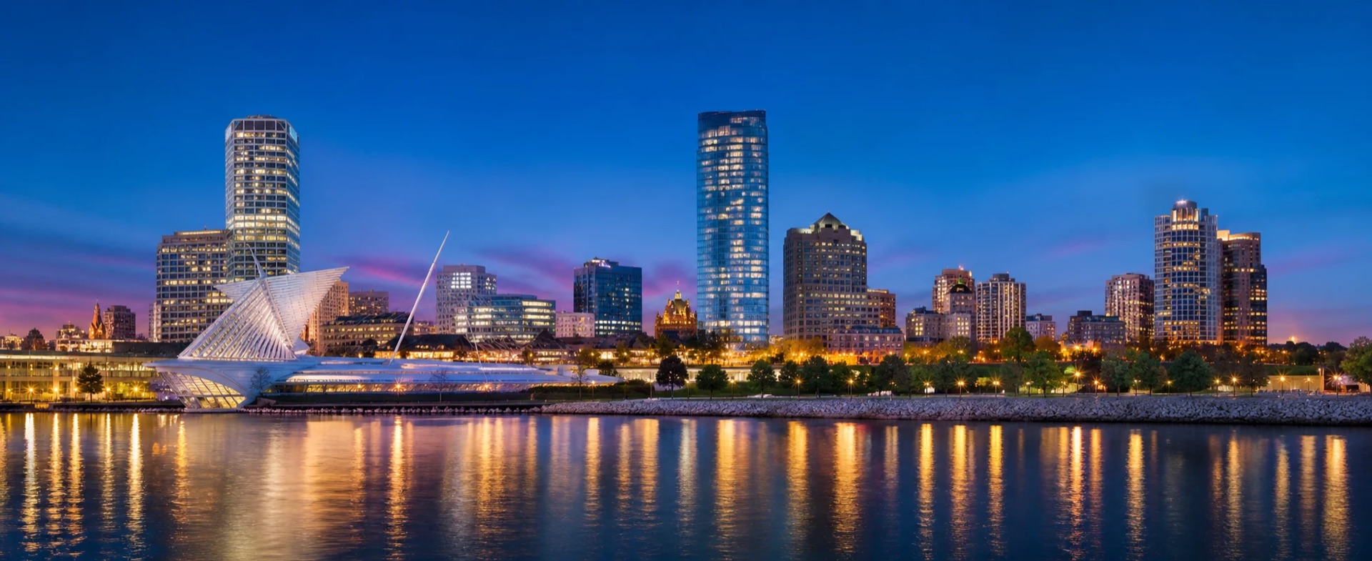 Milwaukee skyline at blue hour — the Milwaukee Art Museum and downtown towers reflected in Lake Michigan